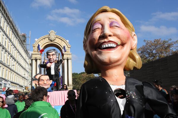 An artist dressed as former French presidential candidate for the far-right National Front (FN) party Marine Le Pen (R) walks ahead of a float depicting the then-French candidate for the left-wing French Socialist (PS) party Benoit Hamon and candidate for the right-wing Les Republicains (LR) party Francois Fillon in the streets of Nice during the 133rd edition of the Nice Carnival on February 19, 2017, in Nice, southeastern France. - Sputnik International