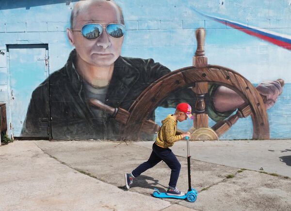 A boy rides a scooter next to graffiti depicting Russian President Vladimir Putin on the embankment of Yalta. - Sputnik International