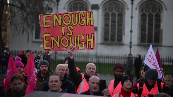 A demonstrator holds a sign reading 'Enough is Enough' as they take part in a rally organised by the Communication Workers Union (CWU), in support of Royal Mail postal workers who are on strike, in Parliament Square in central London on December 9, 2022. - Sputnik International