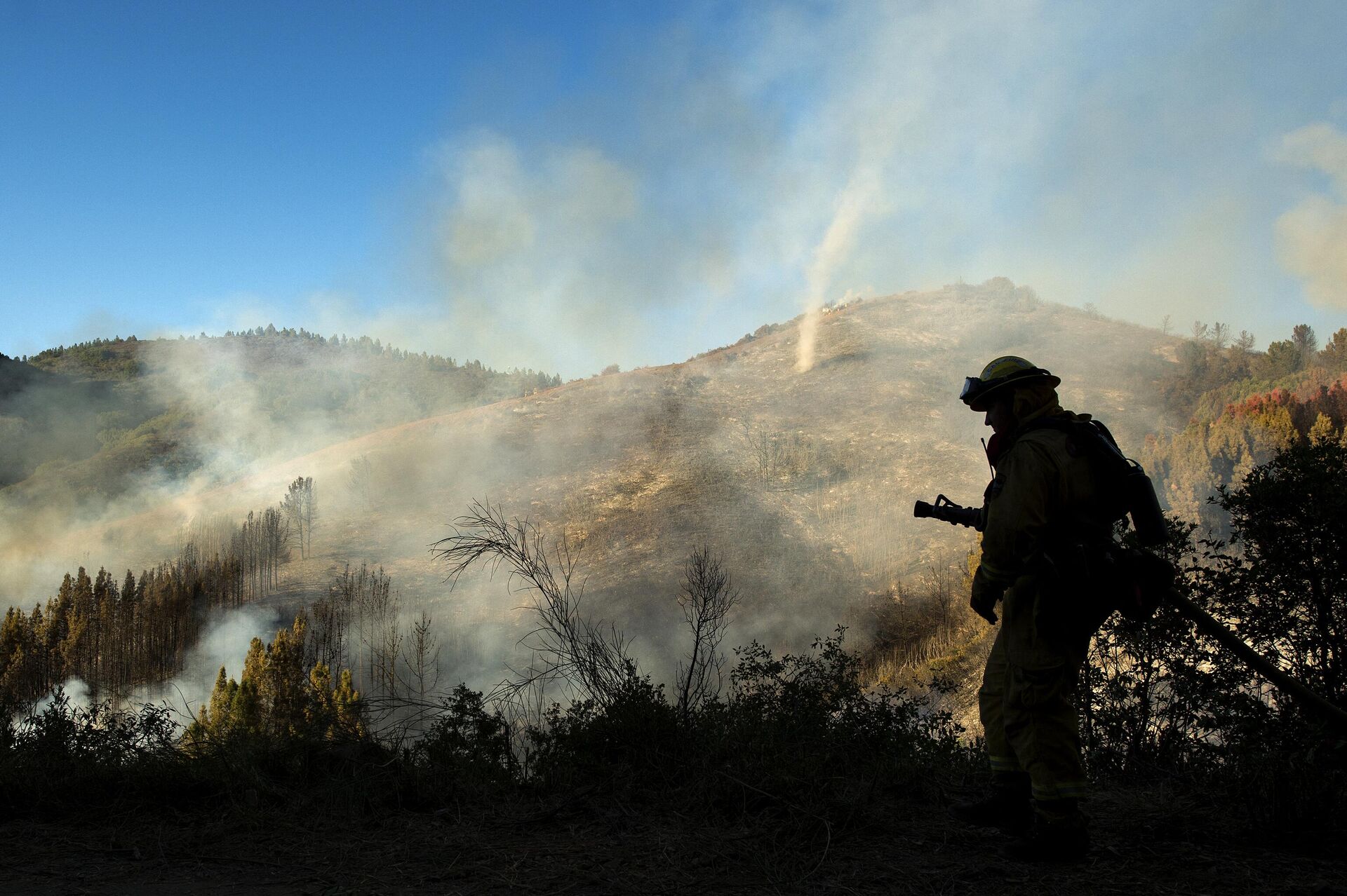 A firefighter walks with a hose as a dust devil kicks up along a charred hillside in the Santa Cruz Mountains near Morgan Hill, California on September 27, 2016.  - Sputnik International, 1920, 14.12.2022