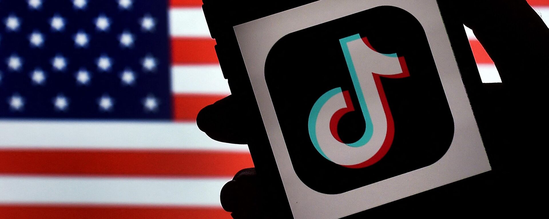The social media application logo, TikTok is displayed on the screen of an iPhone on an American flag background.  - Sputnik International, 1920, 03.01.2023
