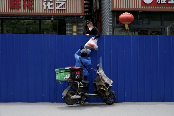 A delivery worker passes items to a man inside a fenced residential area under a COVID-19 lockdown in Beijing on May 11, 2022. - Sputnik International