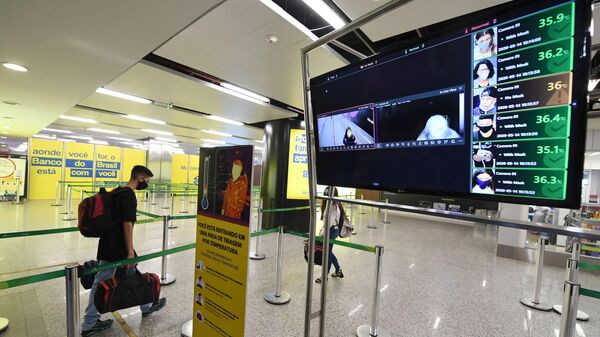 A passenger walks next to a screen showing body temperatures monitored with a camera at the airport in Brasilia on May 14, 2020 - Sputnik International