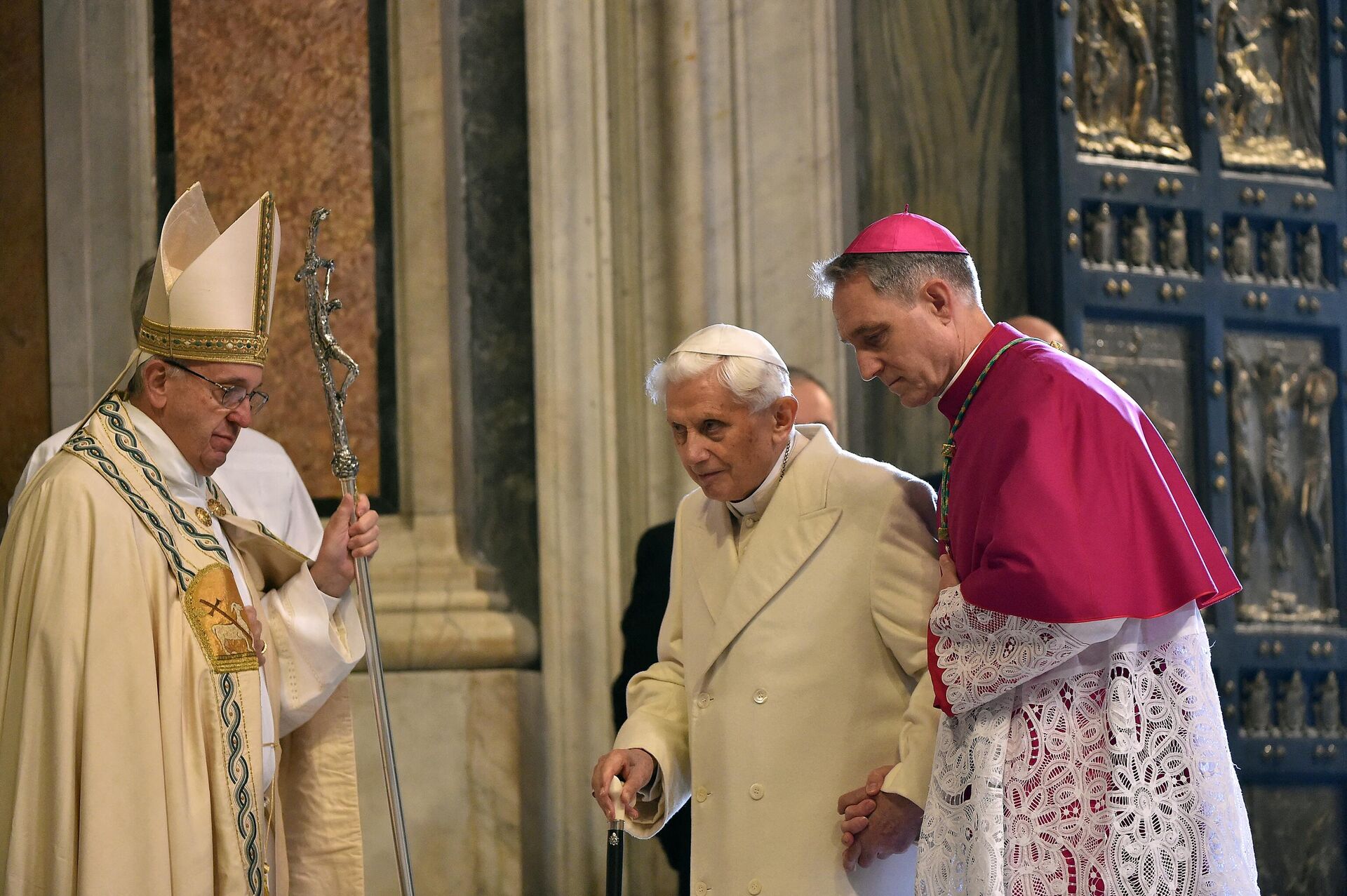 Pope Emeritus Benedict XVI (C) is helped by the prefect of the papal household Georg Gaenswein (R) to pass the Holy Door as Pope Francis (L) looks on, on December 8, 2015 in Vatican. - Sputnik International, 1920, 31.12.2022