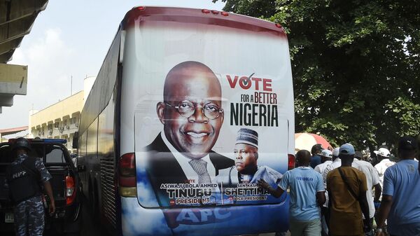 Members of the public stand behind a campaign poster of presidential candidate of All Progressives Congress (APC) Bola Tinubu and runningmate Abdullahi Shettima, displayed on a bus, during a party campaign rally at Teslim Balogun Stadium in Lagos, on November 26, 2022 - Sputnik International