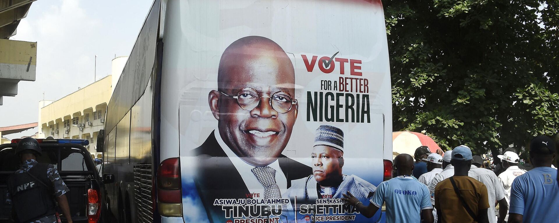 Members of the public stand behind a campaign poster of presidential candidate of All Progressives Congress (APC) Bola Tinubu and runningmate Abdullahi Shettima, displayed on a bus, during a party campaign rally at Teslim Balogun Stadium in Lagos, on November 26, 2022 - Sputnik International, 1920, 29.12.2022