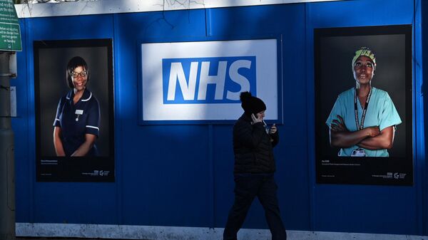 Pedestrians walk past images of workers of Britain's National Health Service (NHS) fixed to hoardings outside a temporary field hospital, set up in the grounds of St George's Hospital in Tooting, south London on January 5, 2022 - Sputnik International