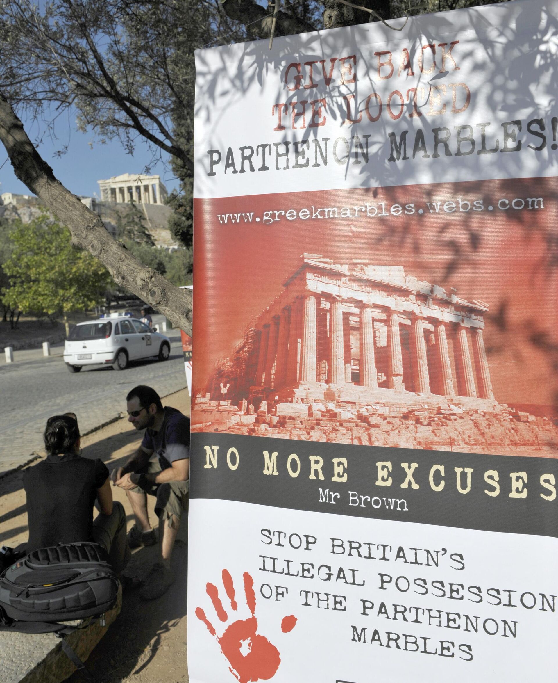 Tourists sit outside the Acropolis hill as a banner reads 'Give back the looted Parthenon marbles, no more excuses, stop Britain's possesion of the Parthenon mables ' during a demonstration in Athens on June 19, 2009.  - Sputnik International, 1920, 05.01.2023