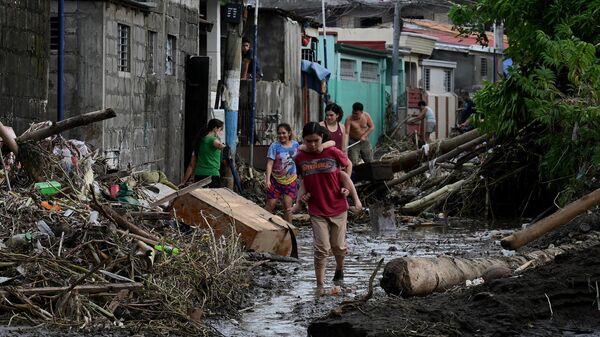 People walk along a mud-covered street in Noveleta, Cavite province on October 30, 2022, a day after Tropical Storm Nalgae hit. - Sputnik International