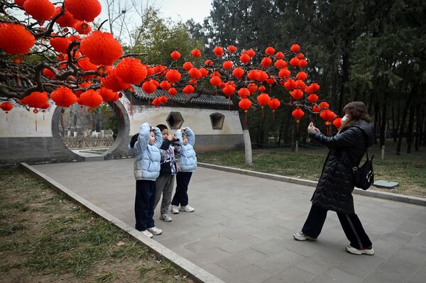 A group of children pose for a picture in front of red lanterns hanging on trees for Chinese Lunar New Year celebrations at a park in Beijing. Red is a main color of Chinese New Year since it is believed to repel evil spirits - Sputnik International