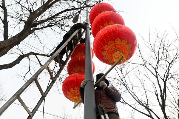Workers hang red lanterns on a light pole along a street for the upcoming Chinese Lunar New Year celebrations in Beijing. - Sputnik International