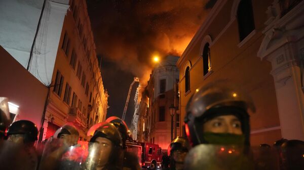 Полиция в защитном снаряжении блокирует улицу на фоне горящего здания во время антиправительственных протестов в Лиме, Перу - Sputnik International