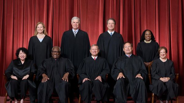 Formal group photograph of the Supreme Court as it was been comprised on June 30, 2022 after Justice Ketanji Brown Jackson joined the Court.  The Justices are posed in front of red velvet drapes and arranged by seniority, with five seated and four standing.

Seated from left are Justices Sonia Sotomayor, Clarence Thomas, Chief Justice John G. Roberts, Jr., and Justices Samuel A. Alito and Elena Kagan. 
Standing from left are Justices Amy Coney Barrett, Neil M. Gorsuch, Brett M. Kavanaugh, and Ketanji Brown Jackson. - Sputnik International