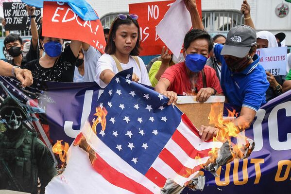 Protesters burn a US flag during a rally in front of the military headquarters in Quezon City, suburban Manila on February 2, 2023, as US Secretary of Defense Llyod Austin and his Philippine counterpart Carlito Galves held a bilateral meeting.(Photo by Ted ALJIBE / AFP) - Sputnik International