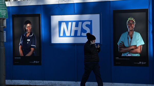 Pedestrians walk past images of workers of Britain's National Health Service, south London, January 5, 2022 - Sputnik International