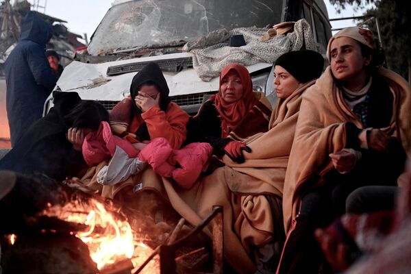 People sit near a bonfire amidst the rubble of collapsed buildings in Kahramanmaras after a 7,8-magnitude earthquake struck southeast Turkiye. Searchers were still pulling survivors on February 8 from the rubble of the earthquake that killed over 15,000 people in Turkey and Syria, even as the window for rescues narrowed.  - Sputnik International