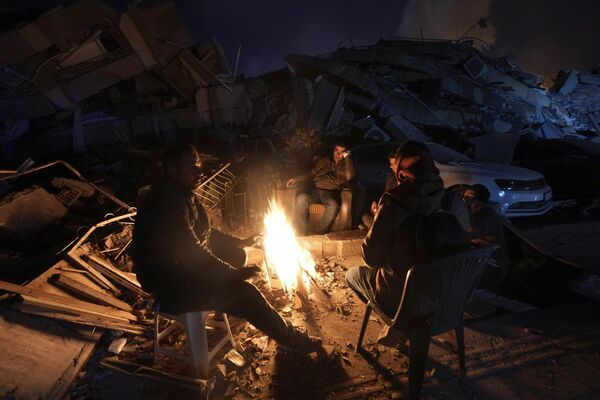 People warm up by a fire in front of destroyed buildings in Antakya, southern Turkiye.   - Sputnik International