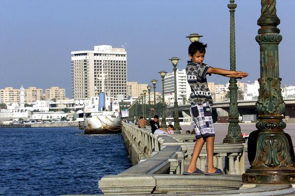 A Libyan boy dances on the wall between the sea front promenade and the harbor of Tripoli on 19 August 2000.  - Sputnik International