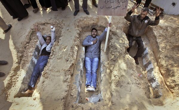 Residents lie in open graves and make the victory sign, to show their willingness to sacrifice themselves to the cause at a park in the main square in Zawiya, 30 miles (50 kilometers) west of Tripoli, in Libya on Sunday 27 February 2011. The placard bears the message: &quot;There is no God but Allah. Martyrs are God&#x27;s beloved.&quot; - Sputnik International