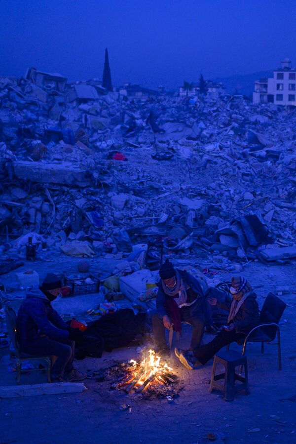 Local residents sitting by a bonfire near the rubble of collapsed buildings in Turkish Hatay province await news of their relations on 14 February 2023, after a 7.8-magnitude earthquake struck the country&#x27;s south-east. - Sputnik International