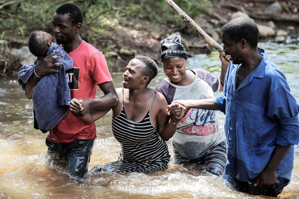 A woman (C/L) with her new born baby (L) crosses a collapsed bridge on Mhlambanyatsi river after the floods which severely affected Nkomazi municipality, in Mpumalanga on February 16, 2023. - Sputnik International