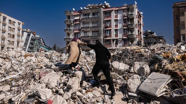 A couple climbs the rubble of collapsed buildings in Antakya, southern Turkey on February 20, 2023. - Sputnik International