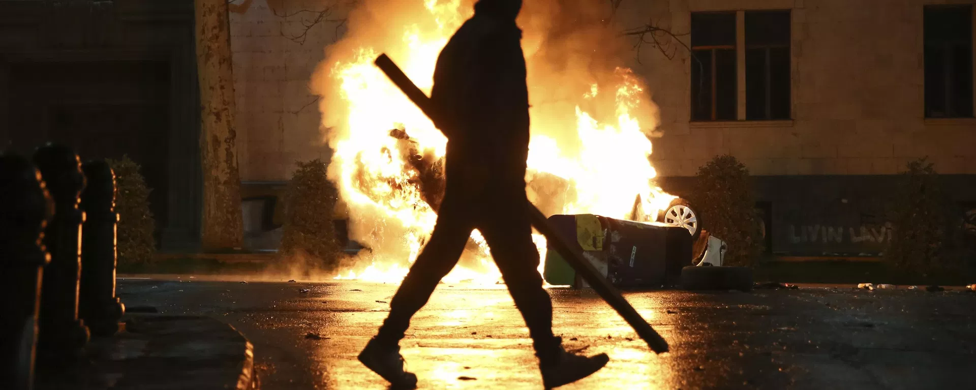 A man with a stick in hand walks past a burning police car not far from the Georgian parliament building in Tbilisi, Georgia, Thursday, March 9, 2023. A man with a stick in hand walks past a burning police car not far from the Georgian parliament building in Tbilisi, Georgia, Thursday, March 9, 2023. - Sputnik International, 1920, 21.05.2024