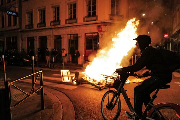 A local resident rides his bike past a fire during a demonstration after the French government pushed pension reform through parliament without a vote, invoking Article 49,3 of the constitution, in Lyon on 16 March 2023. - Sputnik International