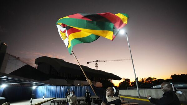 A nun celebrates while holding a Zimbabwean flag to welcome the Zimbabwean high school World and European moot court competition champions as they arrive back at the Robert Mugabe International airport in Harare, Thursday,  July, 7, 2022.  - Sputnik International