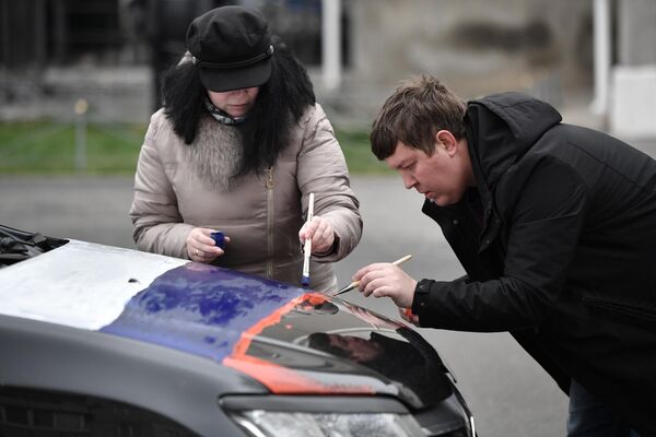 A man and woman paint the hood of a car in the colors of the tricolor at the start of a motor rally dedicated to the 9th anniversary of the reunification of the Republic of Crimea and Sevastopol with Russia in Simferopol. - Sputnik International