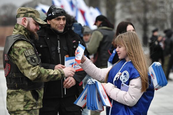 A member of the &quot;Volunteers of Victory&quot; movement hands out flags to participants of a motor rally in Simferopol to mark the 9th anniversary of the reunification of Crimea and Sevastopol with Russia. - Sputnik International