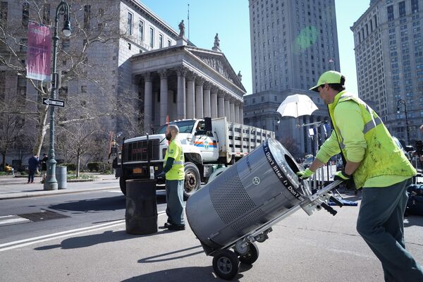 New York City sanitation workers remove trash cans from the street ahead of a possible announcement of a criminal indictment of former President Donald Trump on Monday.  - Sputnik International
