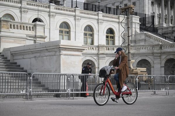 A US Capitol police officer looks on as a person rides a bicycle past barricades and a security camera at the US Capitol in Washington, DC. - Sputnik International