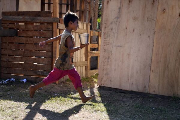 A child, who was displaced from his home by the rising waters of the Paraguay River runs past carrying a container filled with water, on the grounds of his temporary shelter, in Asuncion, Paraguay, Saturday, March 18, 2023. (AP Photo/Jorge Saenz) - Sputnik International