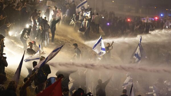 Israeli police use a water cannon to disperse demonstrators blocking a highway during a protest against plans by Prime Minister Benjamin Netanyahu's government to overhaul the judicial system in Tel Aviv, Israel, Monday, March 27, 2023. - Sputnik International