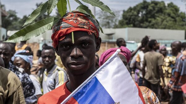A demonstrator with foliage on to his head, a sign of compassion in Central African Republic, holds a Russian flag with the emblem of Russia on while posing for a portrait in Bangui, on March 22, 2023 during a march in support of Russia and China's presence in the Central African Republic. - Sputnik International