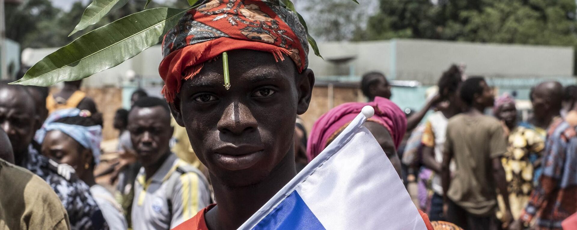 A demonstrator with foliage on to his head, a sign of compassion in Central African Republic, holds a Russian flag with the emblem of Russia on while posing for a portrait in Bangui, on March 22, 2023 during a march in support of Russia and China's presence in the Central African Republic. - Sputnik International, 1920, 26.03.2023