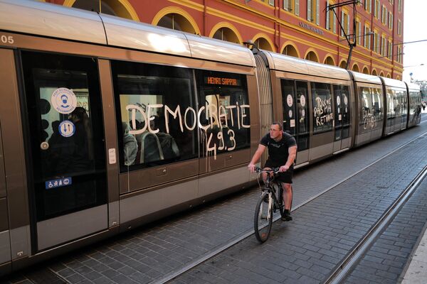 A man cycles past a message that reads, &#x27;Democracy 49.3&#x27;, daubed on the side one a tram carriage as demonstrations take place across France.  - Sputnik International