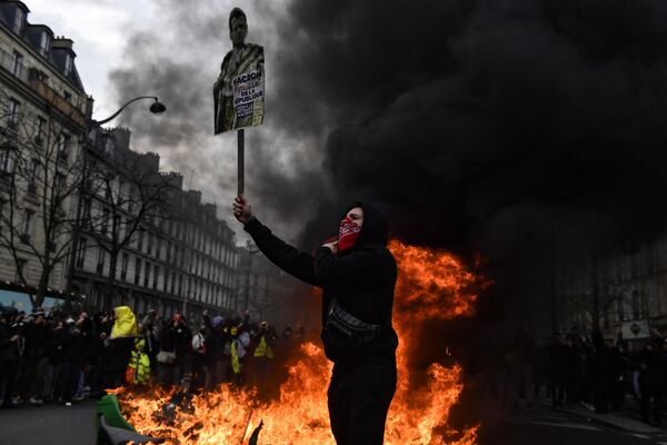 A protester holds a portrait of French President Emmanuel Macron next to a fire ready to burn it.  - Sputnik International