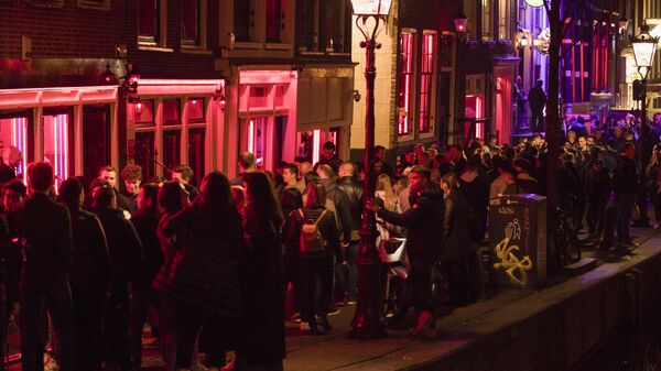In this Friday March 29, 2019, file image tourists bathing in a red glow emanating from the windows and peep shows' neon lights are packed shoulder to shoulder as they shuffle through the alleys in Amsterdam's red light district, Netherlands. - Sputnik International