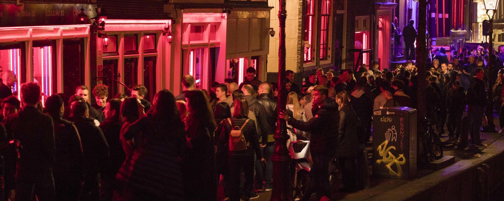 In this Friday March 29, 2019, file image tourists bathing in a red glow emanating from the windows and peep shows' neon lights are packed shoulder to shoulder as they shuffle through the alleys in Amsterdam's red light district, Netherlands. - Sputnik International, 1920, 29.03.2023