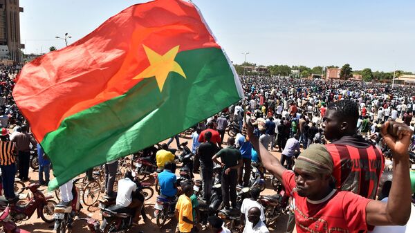 A man holds up the national flag as people celebrate at the Place de la Nation in the capital Ouagadougou, after Burkina Faso's embattled President Blaise Compaore announced earlier on October 31, 2014, he was stepping down to make way for elections following a violent uprising against his 27-year rule - Sputnik International
