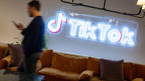 In this file photo taken on February 09, 2022 an employee looks at his mobile phone as he walks past the logo of the video-focused social networking service TikTok, at the TikTok UK offices, in London - Sputnik International