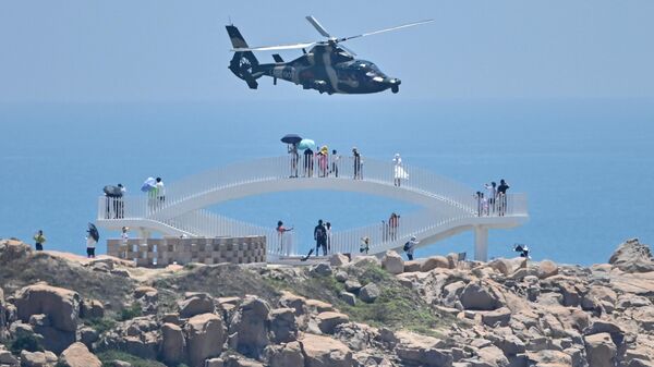 Tourists look on as a Chinese military helicopter flies past Pingtan island, one of mainland China's closest point from Taiwan, in Fujian province on August 4, 2022 - Sputnik International