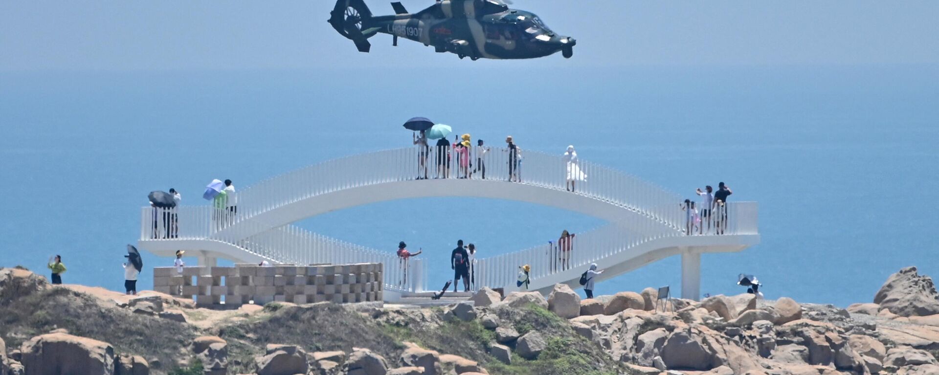 Tourists look on as a Chinese military helicopter flies past Pingtan island, one of mainland China's closest point from Taiwan, in Fujian province on August 4, 2022 - Sputnik International, 1920, 09.04.2023