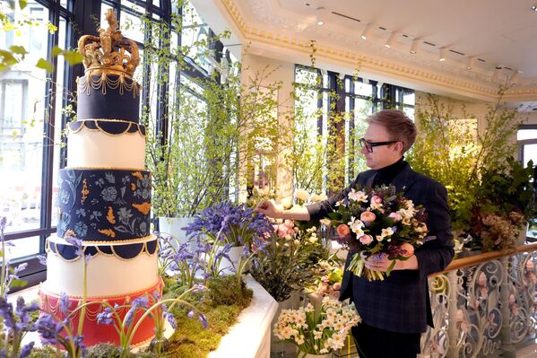 Philip Hamond, designer florist at the Dorchester Hotel, works alongside a display showing a Coronation themed cake and floral arrangements in London. The Dorchester Hotel, long a favorite with royals and celebrities, concocted a lavish, five-tier coronation cake and put up theater-style draping across its facade to re-create the decorations that it used to mark Queen Elizabeth II’s coronation in 1953 in preparation for King Charles III&#x27;s coronation.  - Sputnik International
