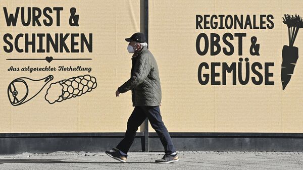 A man wearing a face protection mask walks past a grocery store advertising meat products and ham (L) and fruits and vegetables (R) in Berlin. File photo. - Sputnik International