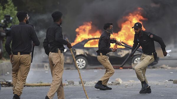 Policemen retreat after firing teargas shells towards Pakistan Tehreek-e-Insaf (PTI) party activists and supporters of former Pakistan's Prime Minister Imran Khan near a burning car during a protest against the arrest of their leader in Karachi on May 9, 2023 - Sputnik International