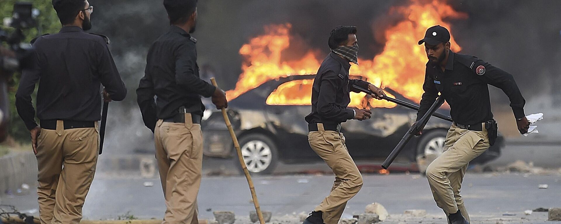 Policemen retreat after firing teargas shells towards Pakistan Tehreek-e-Insaf (PTI) party activists and supporters of former Pakistan's Prime Minister Imran Khan near a burning car during a protest against the arrest of their leader in Karachi on May 9, 2023 - Sputnik International, 1920, 10.05.2023