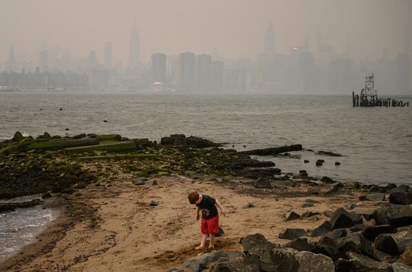 A child stands on the shore before the New York City skyline and East River shrouded in smoke in Brooklyn on June 6, 2023. Smoke from wildfires blazing in eastern Canada has drifted south. According to the Canadian Interagency Forest Fire Center, on June 6, 2023, hundreds of wildfires were burning in Canada, as fires have broken out across the country in recent weeks. Quebec alone had more than 150 active blazes across the province, the fire agency said. - Sputnik International